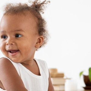 Bebê de perfil sorrindo e vestindo blusa branca