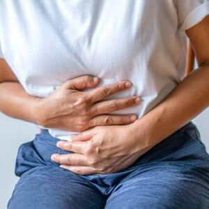 mulher com usando camiseta branca, levemente curvada e com as mãos posicionadas na barriga