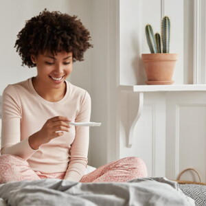 Mulher sentada na cama olhando feliz para um teste de gravidez