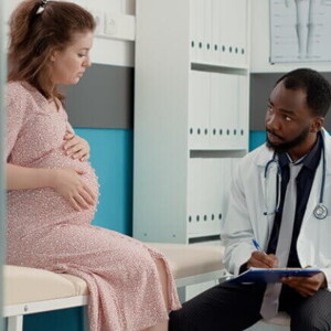 Gestante sentada sobre uma maca conversa com um médico sentado na sua frente