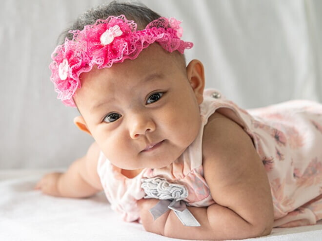 Ensaio fotográfico de bebê que se chama Alice com laço rosa na cabeça.