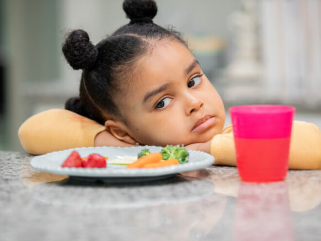 menina com semblante desconfiado olha para prato de comida sem vontade