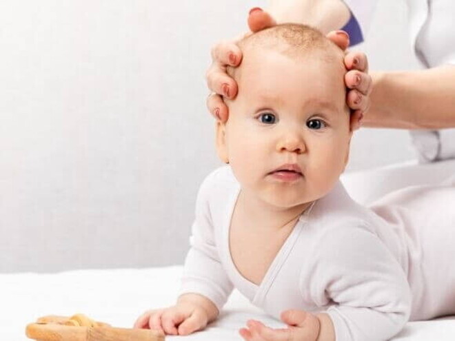 Um bebê deitado com a sua cabeça sendo segurada por duas mãos