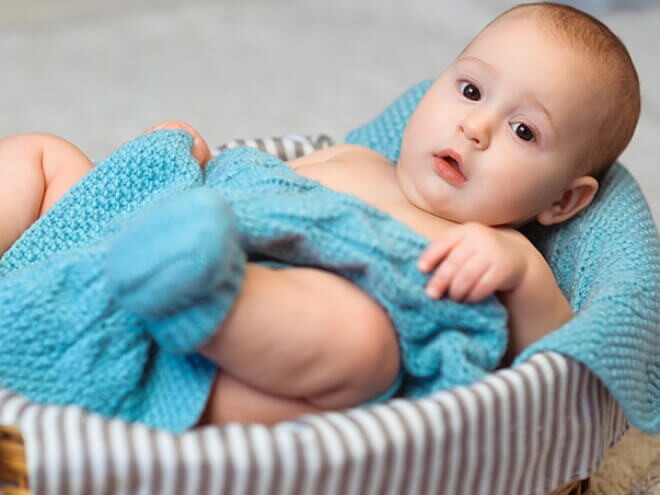 Imagem de um bebê aconchegado em um cobertor azul dentro de uma cesta