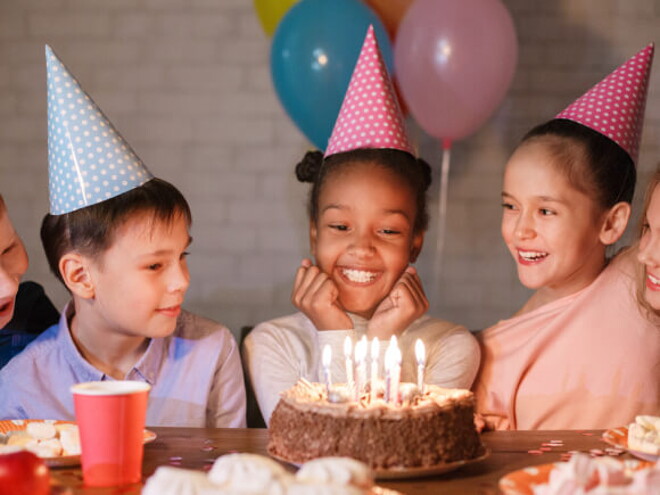 diversas crianças sorriem ao redor de bolo sobre mesa