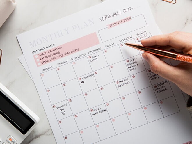 Na imagem, uma mão segura uma caneta diante de um calendário do mês