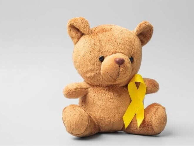 Urso de pelúcia com um laço dourado que simboliza o mês da conscientização sobre o câncer infantil