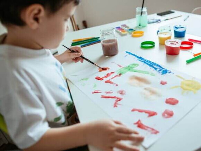 Criança canhota pintando uma folha branca com tinta e pincel