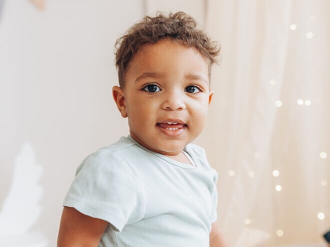 Criança vestindo blusa azul claro em um quarto de cores neutras e luzes de decoração