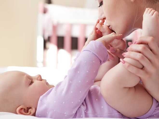 Mãe embalando carinhosamente as perninhas do seu bebê que está deitado na cama