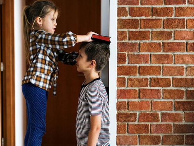 Duas crianças em frente um parede de tijolos brincando de medir a altura