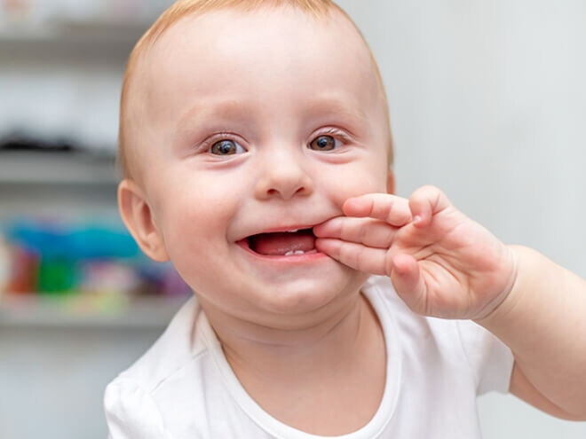 Bebê engatinhando no chão e com a mão na boca sorrindo.