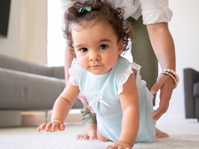 Menina vestindo vestido azul aprendendo a engatinhar