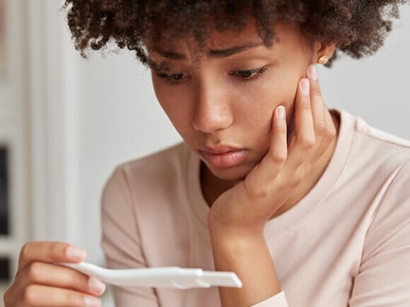 Imagem de mulher aflita olhando para um teste de gravidez