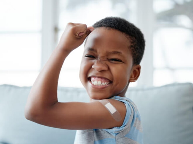 menino feliz sorri com braço levantado e um band-aid