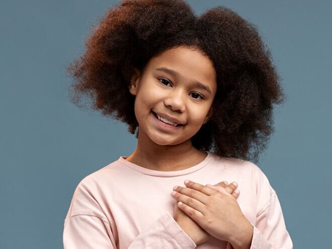 Menina com as duas mãos na região do coração sorrindo