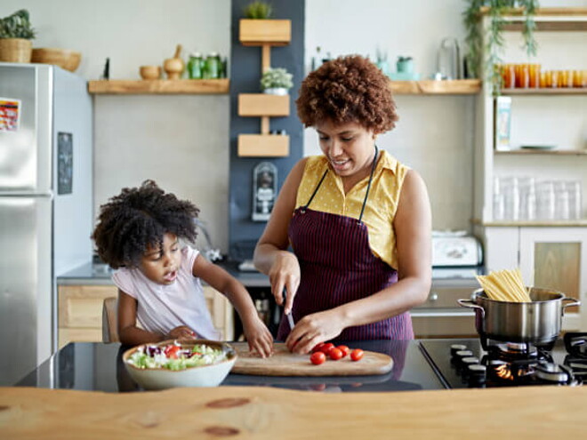 mulher pica legumes sob mesa de cozinha com criança ao lado interagindo