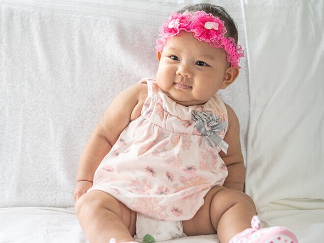 Bebê recém nascida usando vestido florido e laço bordado na cabeça.