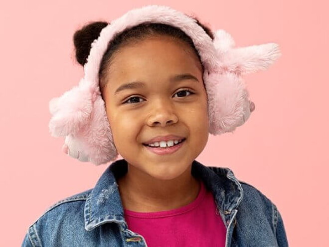 Menina usando jaqueta jeans e protetor de ouvido de pelúcia em frente a uma parede cor de rosa