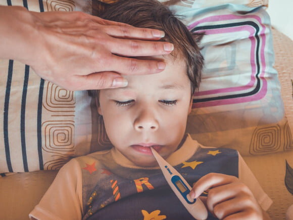 menino com febre com os olhos fechados e termômetro na boca