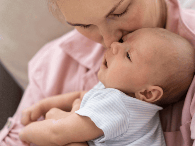 Mãe segurando no colo bebê recém nascido e beijando sua testa.