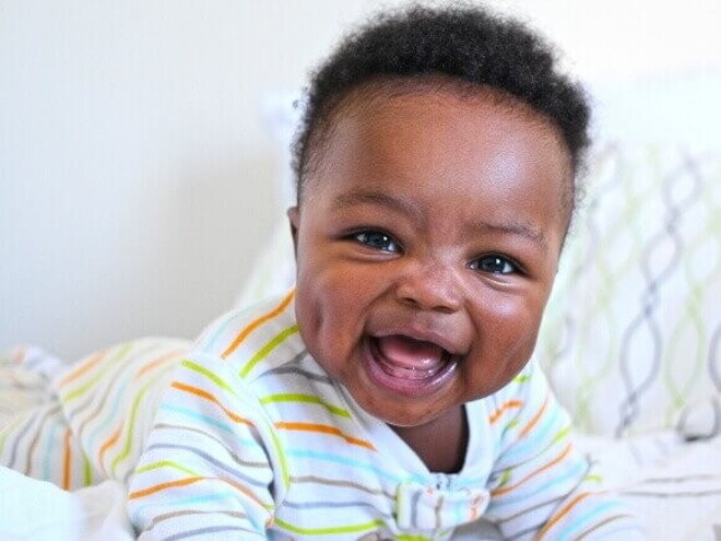 Bebê deitado e sorrindo, deitado em uma cama, sob um fundo branco.