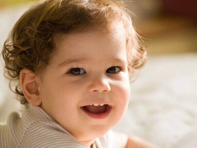 Bebê deitado e sorrindo, sendo iluminado pela luz do sol