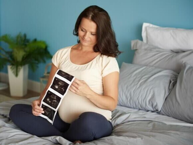 Mulher grávida sentada em uma cama, observando o resultado de um exame de ultrassom