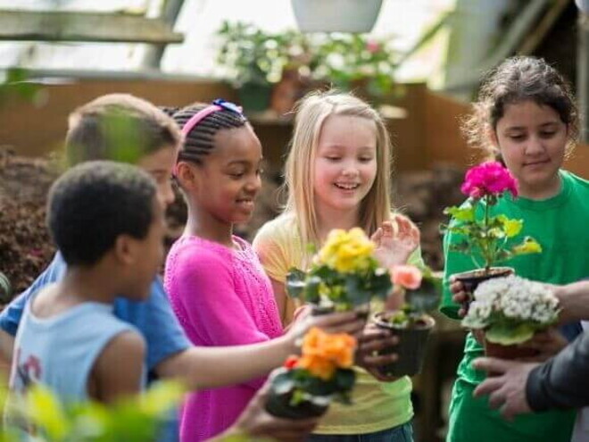 Um grupo de crianças em um jardim comunitário, segurando vasos de plantas coloridas e sorrindo enquanto participam de uma atividade de jardinagem.