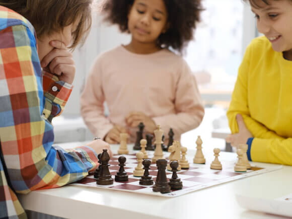 três crianças ao redor de mesa jogando xadrez
