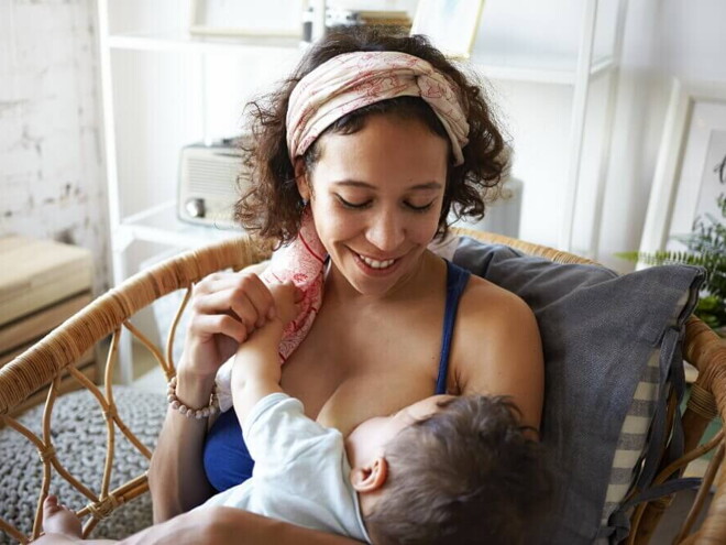 Mãe sentada e sorrindo, amamentando um bebê em seu colo