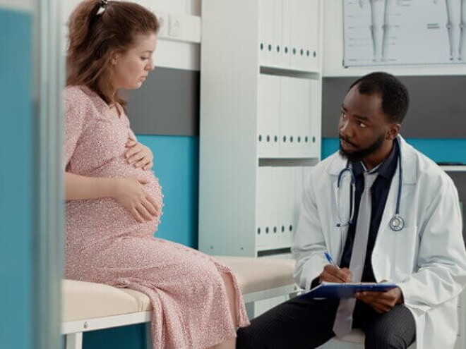 Gestante sentada sobre uma maca conversa com um médico sentado na sua frente