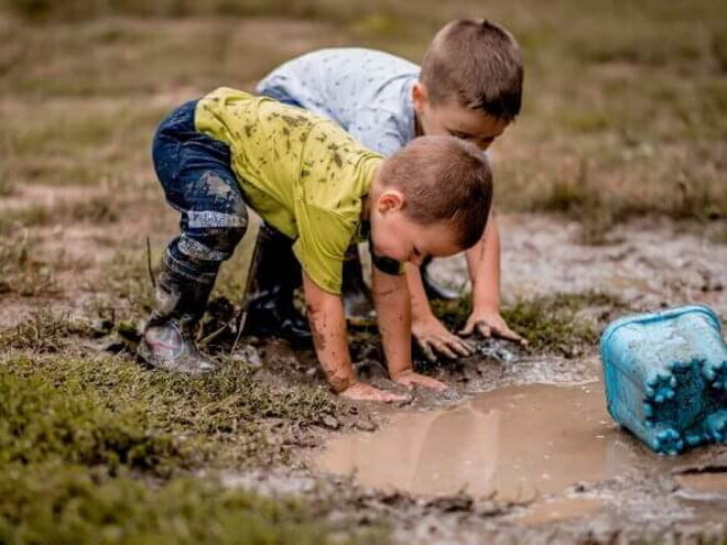 Duas crianças brincando com as mãos na lama e as roupas sujas.