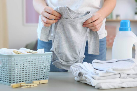 adulto dobrando roupas de bebê nas cores cinza e branco