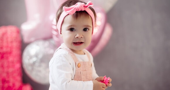 Bebê usando macacão e laço na cabeça sorrindo.