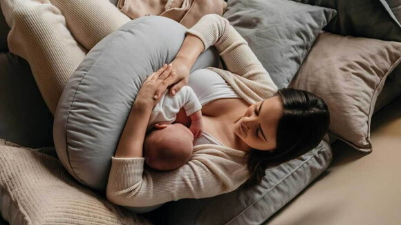 Mulher amamentando bebê que está acomodado em uma almofada de amamentação.