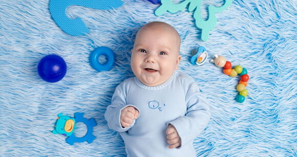 Bebê recém nascido usando roupa azul deitado em cima de um cobertor azul com brinquedos ao redor.