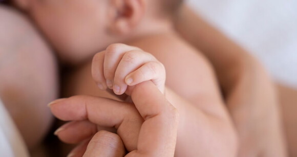 bebê segurando o dedo da mãe enquanto amamenta