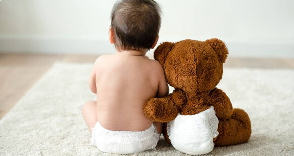 bebê sentado de costas ao lado de um urso de pelúcia