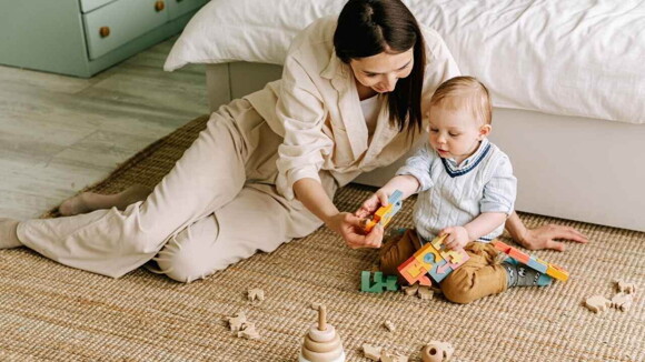 Mãe sentada em um tapete ao lado do bebê com vários brinquedos espalhados