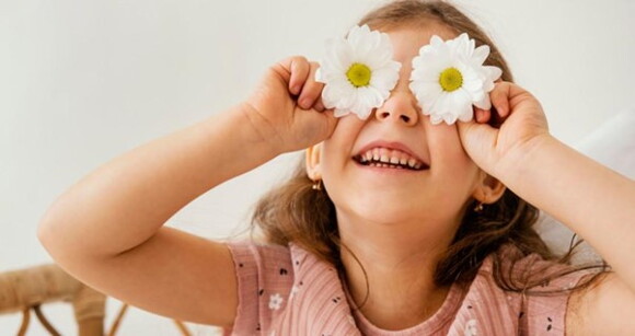 Menina usando camiseta florida rosa sorrindo com flores de margaridas sobre os olhos