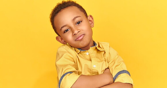 Menino com os braços cruzados vestindo camisa amarela e em um fundo amarelo