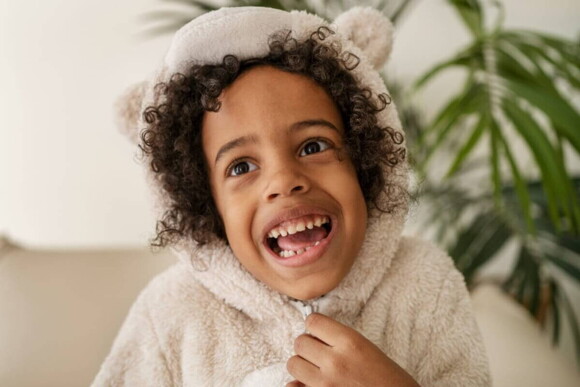 Uma criança vestindo uma roupa de frio com a boca aberta mostrando os dentes.