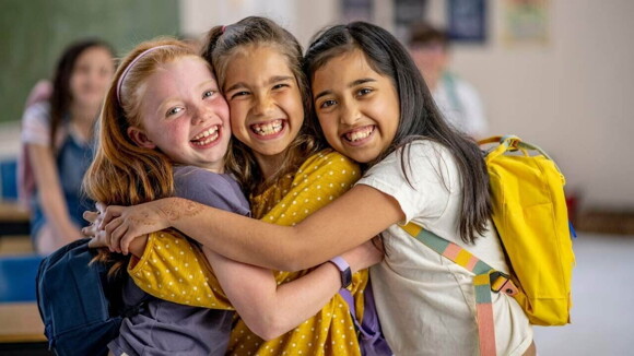 Três meninas abraçadas e sorrindo na sala de aula