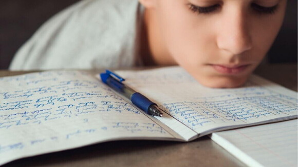 Criança com a cabeça deitada sobre um caderno com aspecto de desânimo