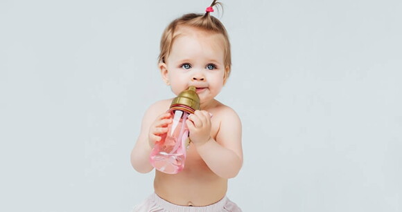 Bebê de olhos azuis com mamadeira na boca.