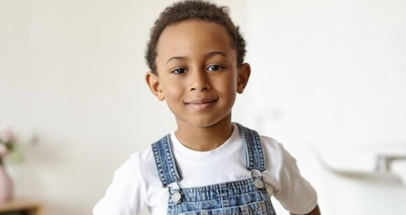 Menino usando macacão jeans e camiseta branca sorrindo