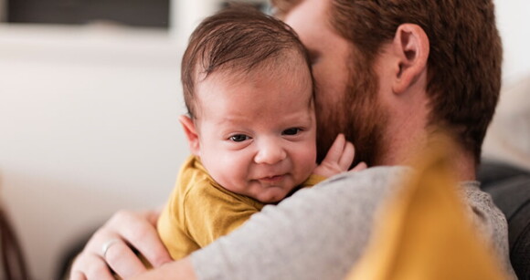 Homem embalando suavemente um bebê nos braços, mostrando o vínculo entre pai e filho