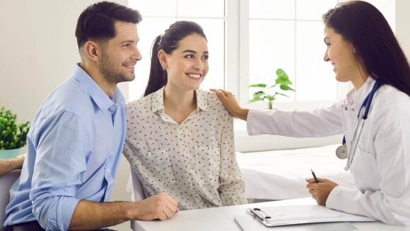 Casal sorridente realizando uma consulta com uma profissional de saúde