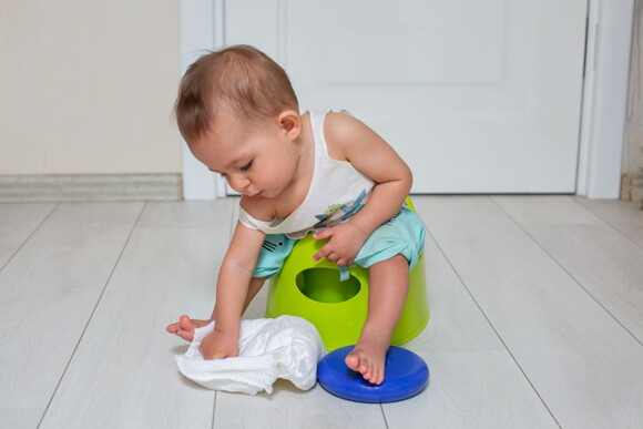 Foto de bebê sentado no penico brincando com uma fralda